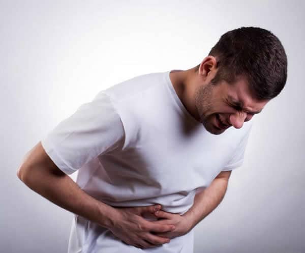 man-in-white-shirt-with-stomach-pain-against-gray-background