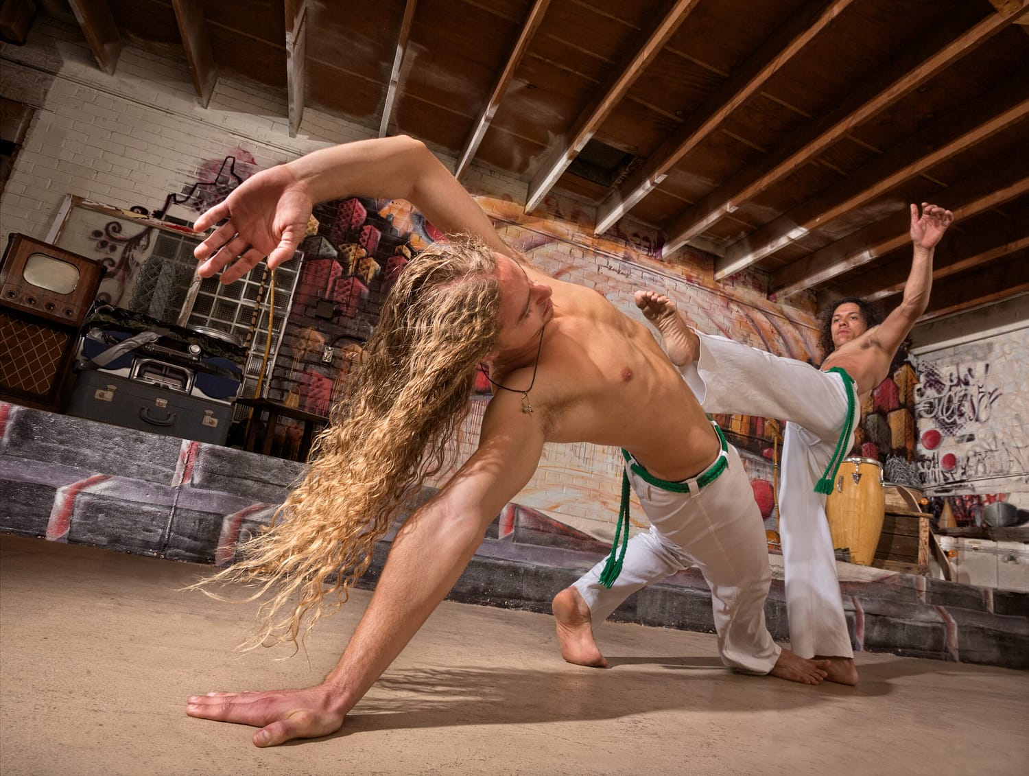 Young male capoeira partners performing kicks indoors